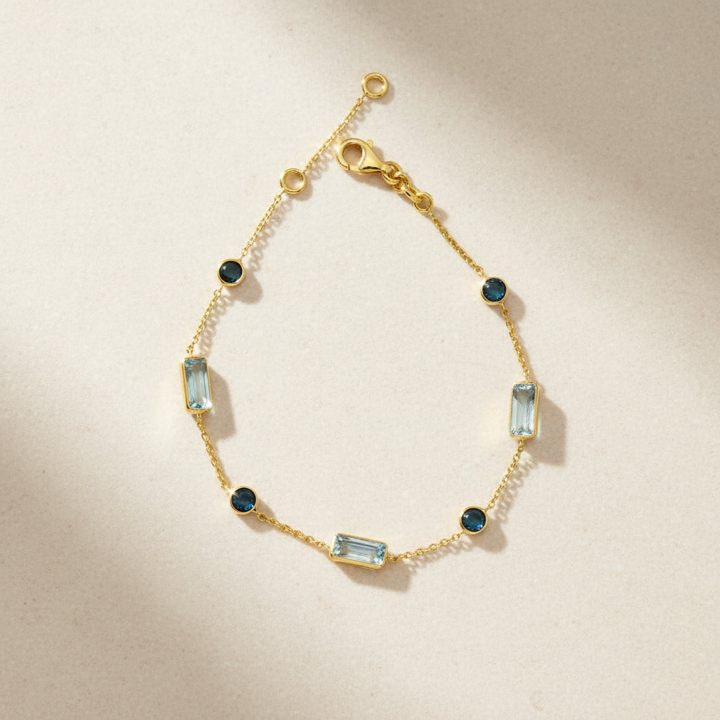 Zartes Gelbgoldarmband mit rechteckigen hellblauen Topasen und runden London Blue Topasen in Zargenfassungen, gleichmäßig entlang der feinen Kette verteilt.