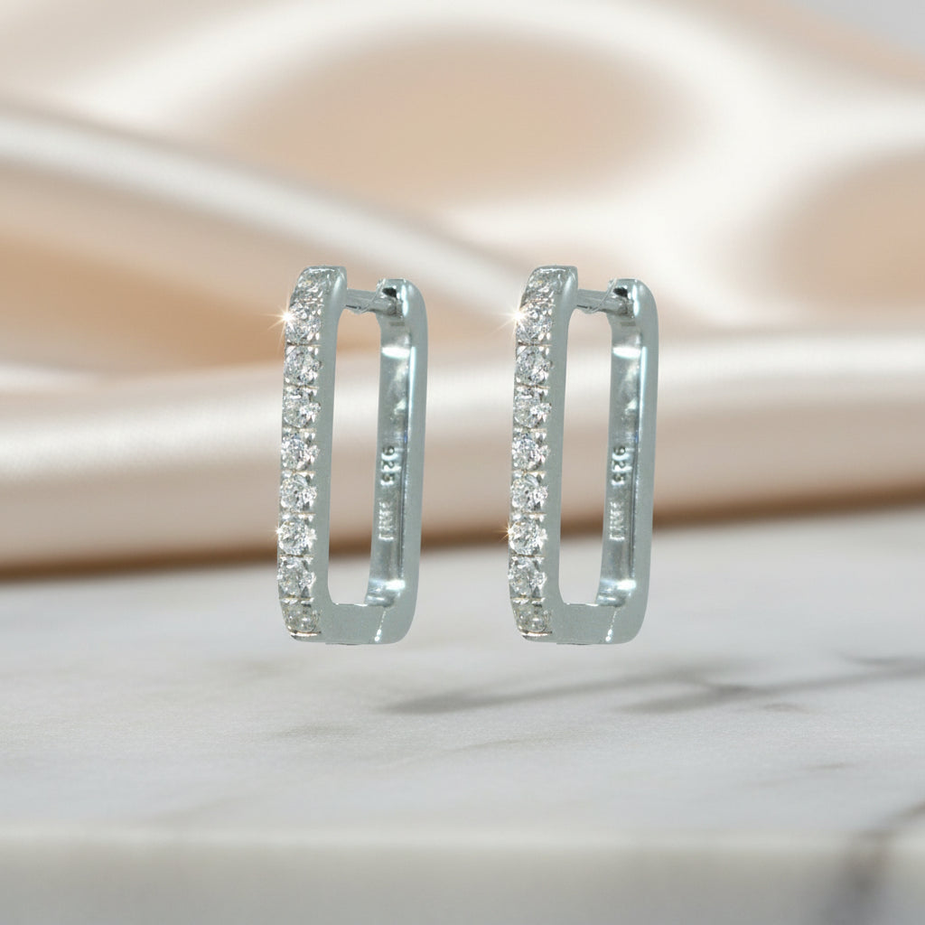 Rechteckige Creolen aus rhodiniertem 925er Silber mit einer Reihe klar funkelnder Zirkonia-Steine auf der Vorderseite.