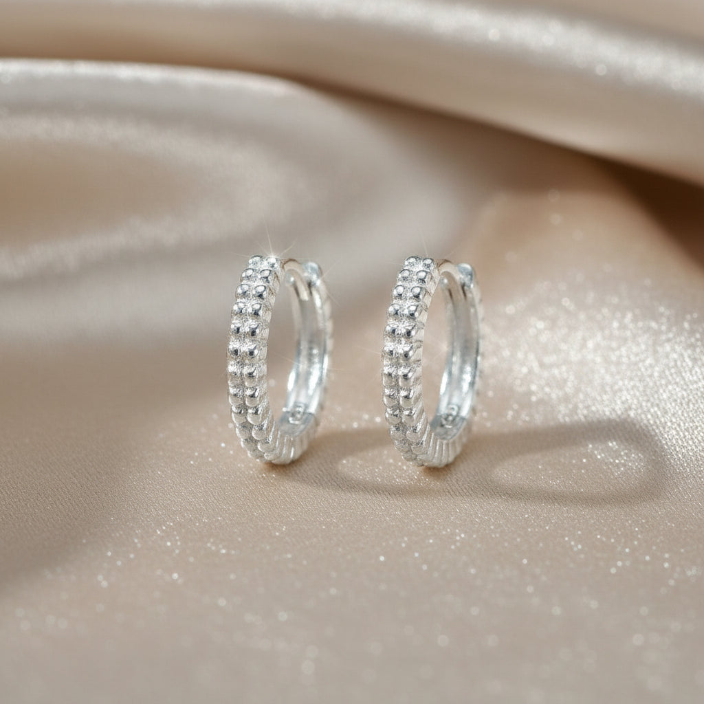 Rundliche Creolen aus rhodiniertem 925er Silber mit umlaufender Oberfläche im feinen Bead-Design.