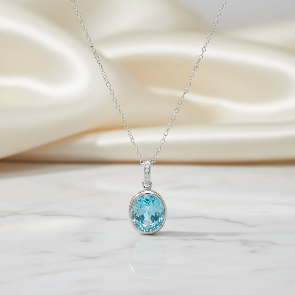 Feine Silberkette mit ovalem, hellblauem Topas-Anhänger in Zargenfassung und mit kleinen, klaren Steinen besetzter Öse.