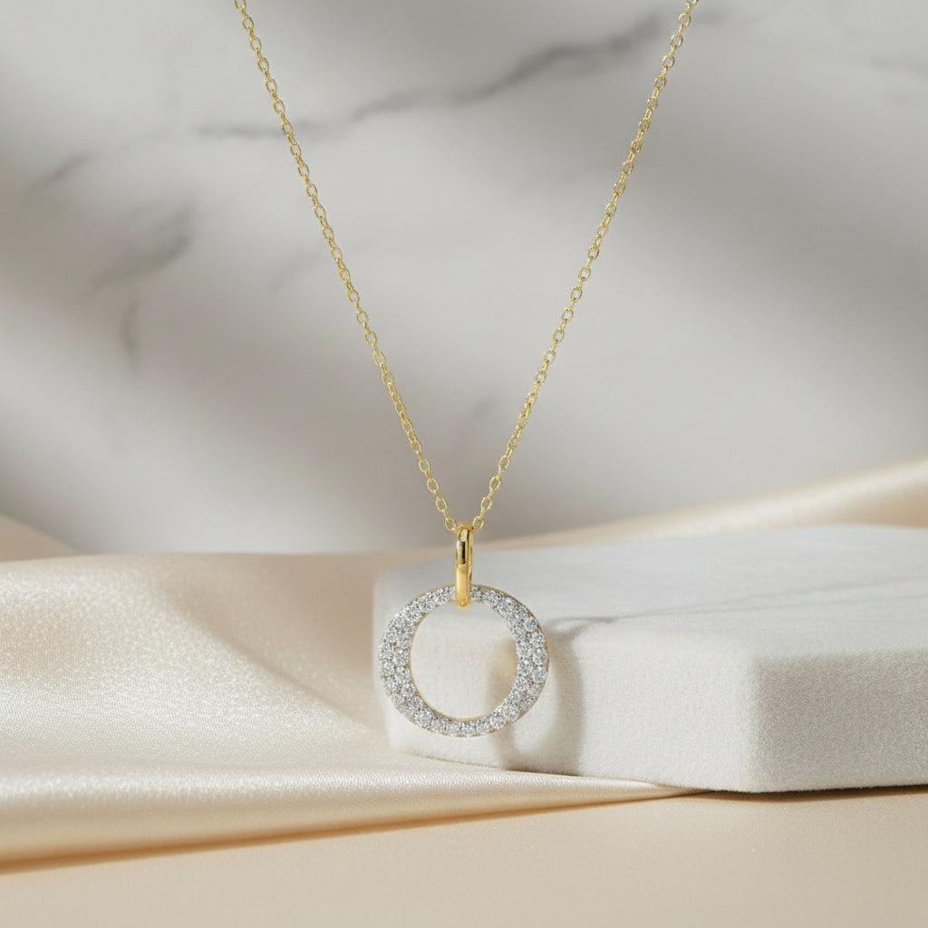 Feine, vergoldete Kette mit rundem Anhänger, dessen Vorderseite vollständig mit klar funkelnden Zirkonia-Steinen besetzt ist.