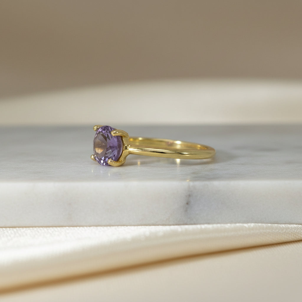 Gelbgoldring mit violettem Amethyst-Solitär in vier Krappen, von schräg seitlich fotografiert.