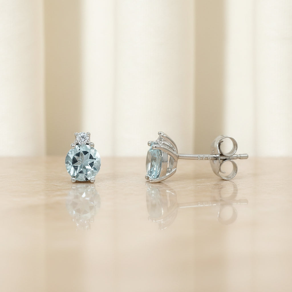 Silberne Ohrstecker mit einem ovalen blauen Topas und einem kleinen Zirkonia-Stein darüber.