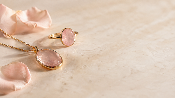 Zartrosa Rosenquarz-Schmuckstein in goldener Fassung auf hellem Marmor — Splendido Schmuck