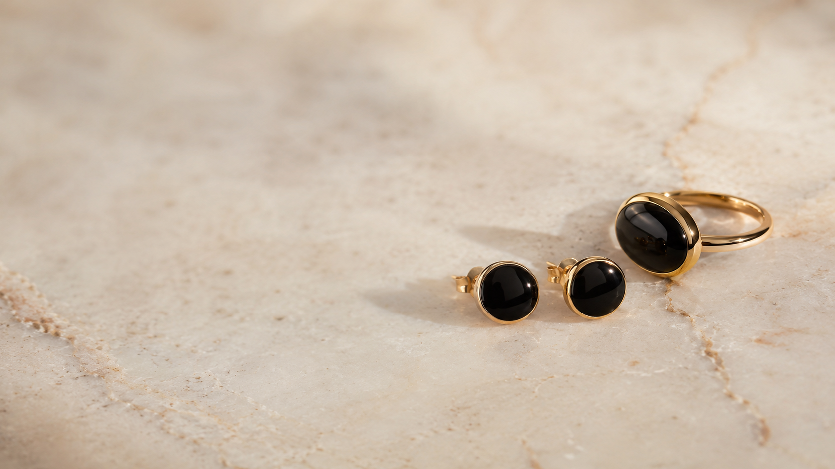 Schwarzer Onyx-Schmuck mit heller Silber- und Goldfassung auf cremefarbenem Hintergrund — Splendido Schmuck