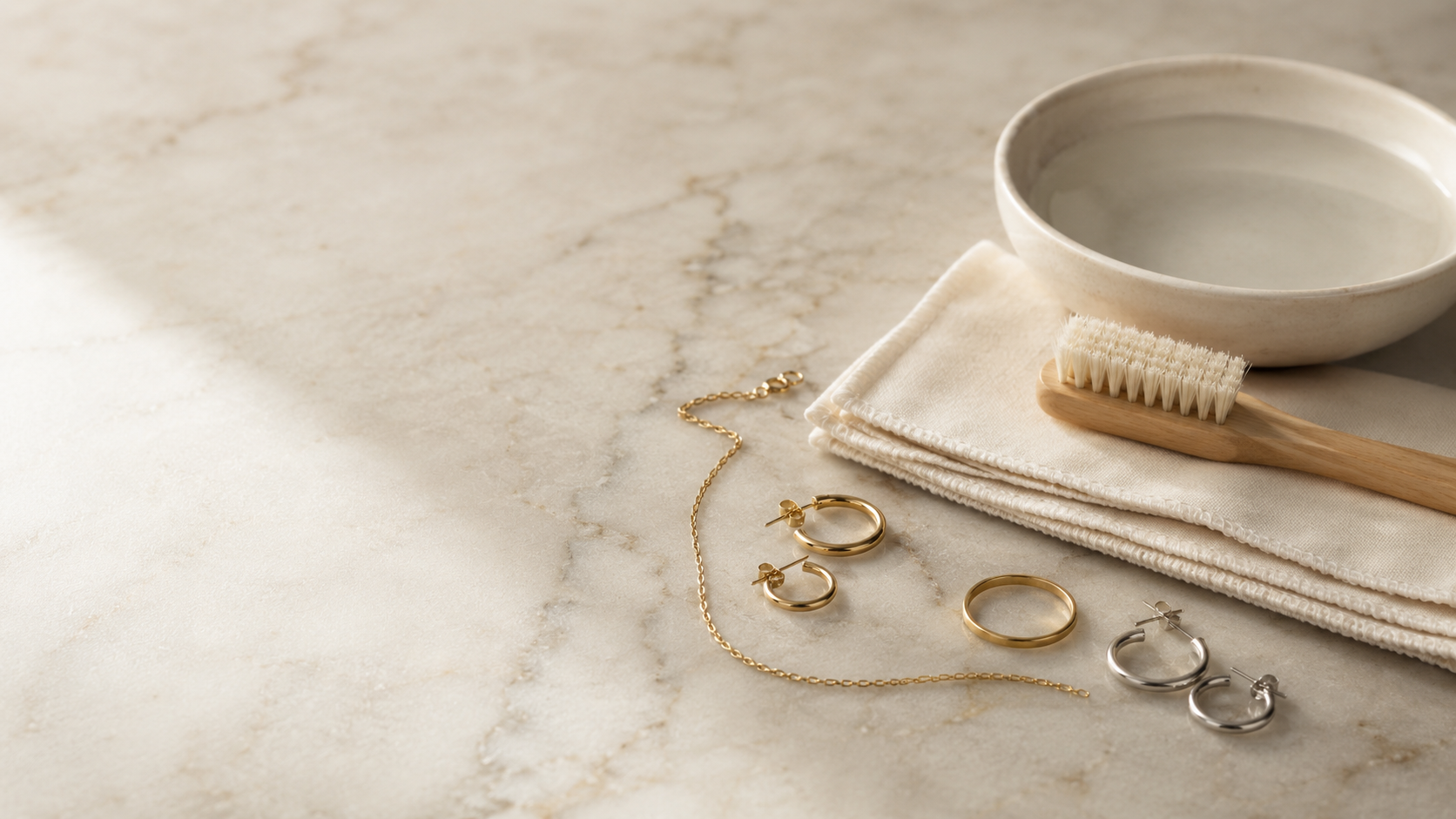 Goldschmuck und Silberschmuck mit Pflegeschale, weichem Tuch und Bürste auf Marmor — Splendido Schmuck