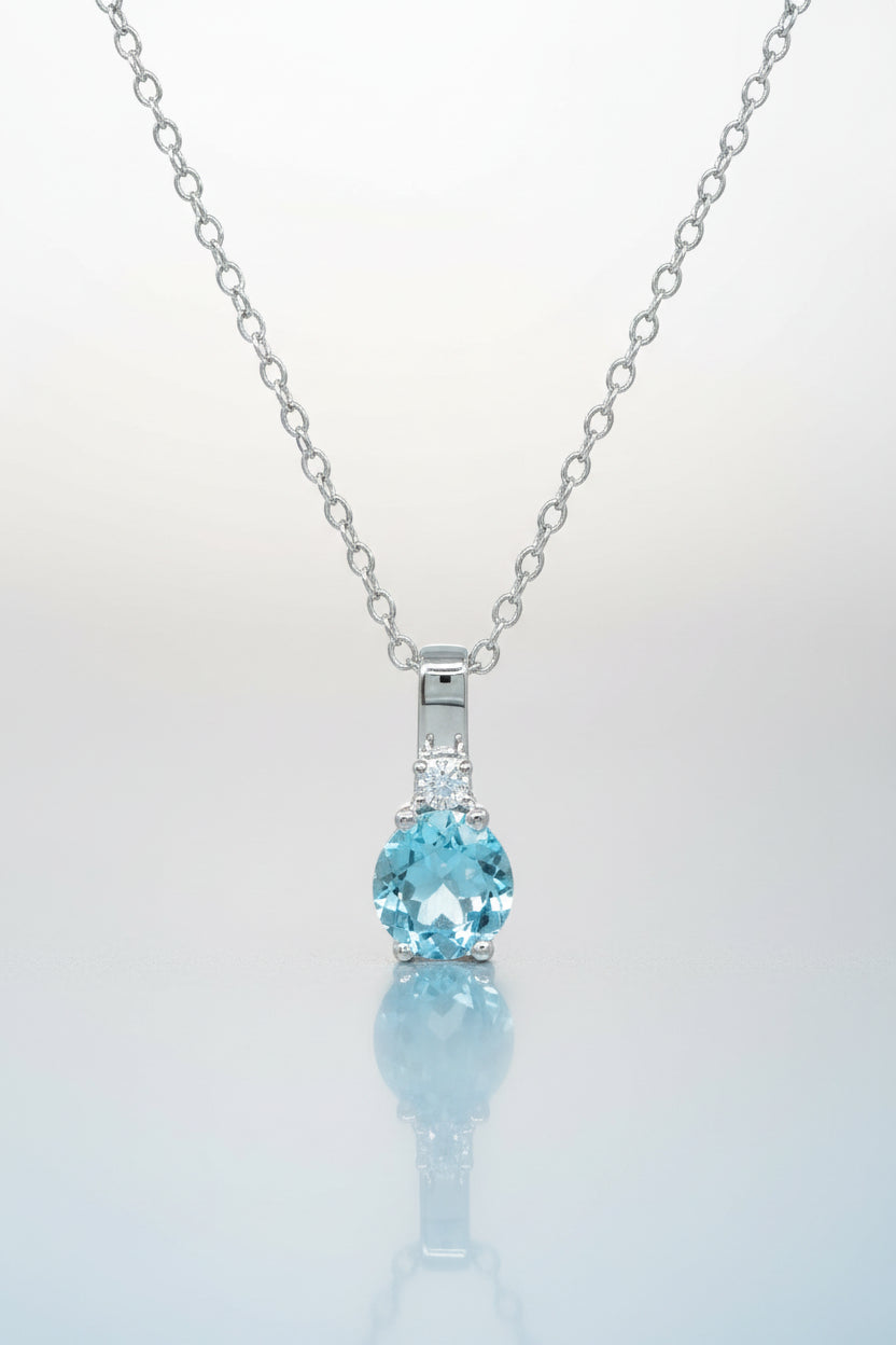 Nahaufnahme eines Silberanhängers mit rund facettiertem blauem Topas und kleinen klaren Steinen an einer feinen Ankerkette.