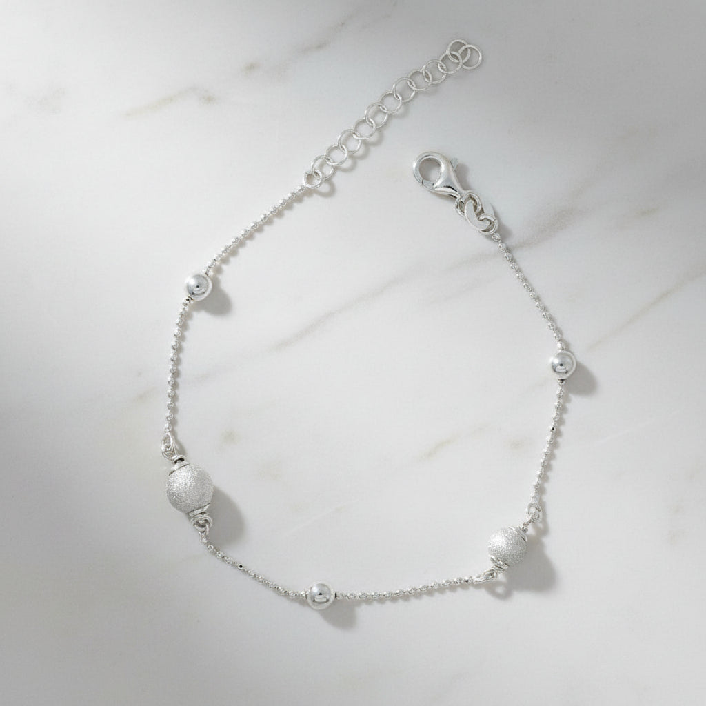 Feines Armband aus rhodiniertem 925er Silber mit zarter Kugelkette und abwechselnd matt strukturierten und polierten Silberkugeln, mit Verlängerungskettchen und Karabinerverschluss.