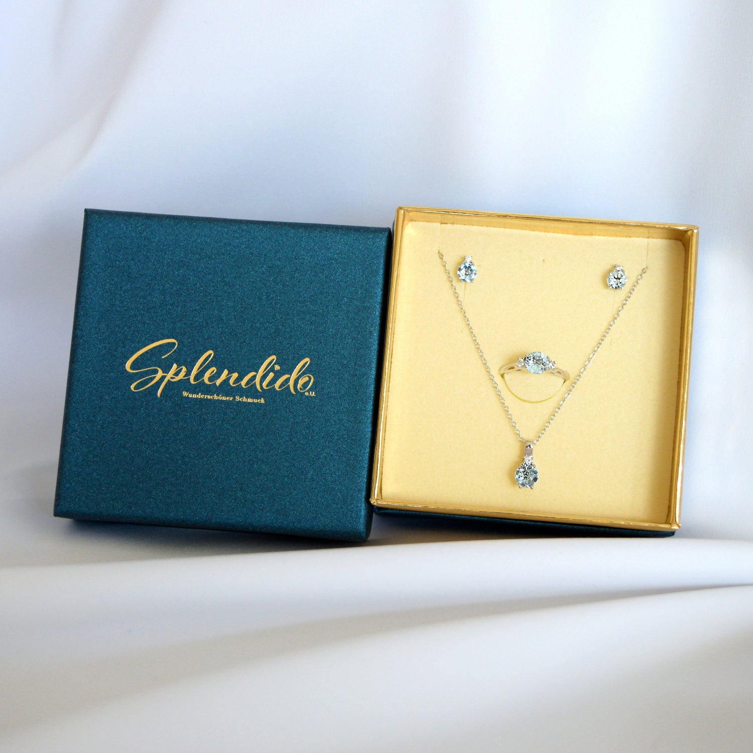 Geschenkverpackung von Splendido in Türkis mit goldfarbenem Innenfutter und Schmuckset aus Kette, Ring und Ohrsteckern
