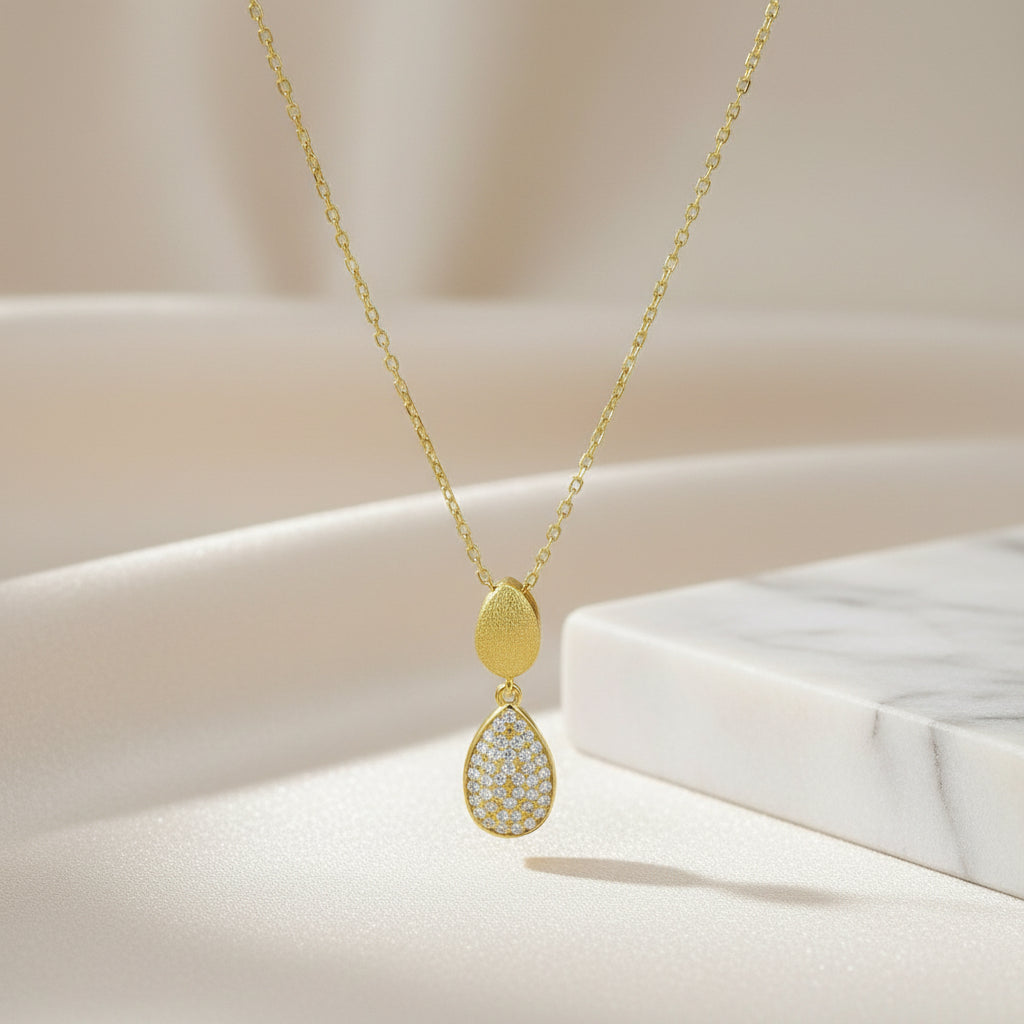 Feine vergoldete Kette mit länglichem Anhänger aus zwei übereinander liegenden Tropfenelementen, das untere dicht mit klaren Zirkonia-Steinen besetzt.
