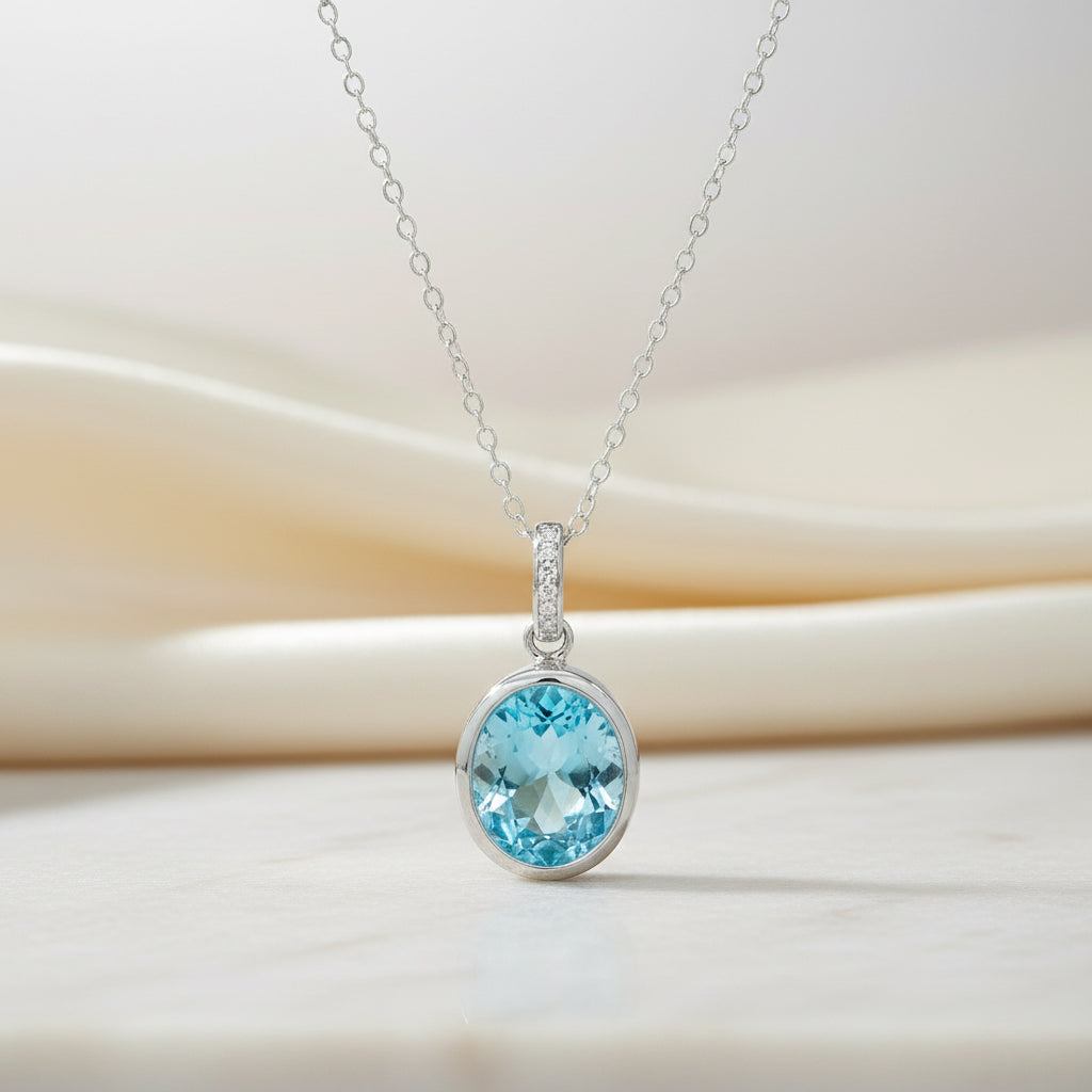 Detailaufnahme eines ovalen, hellblauen Topas in Silber-Zargenfassung mit funkelnd besetzter Anhängeröse.