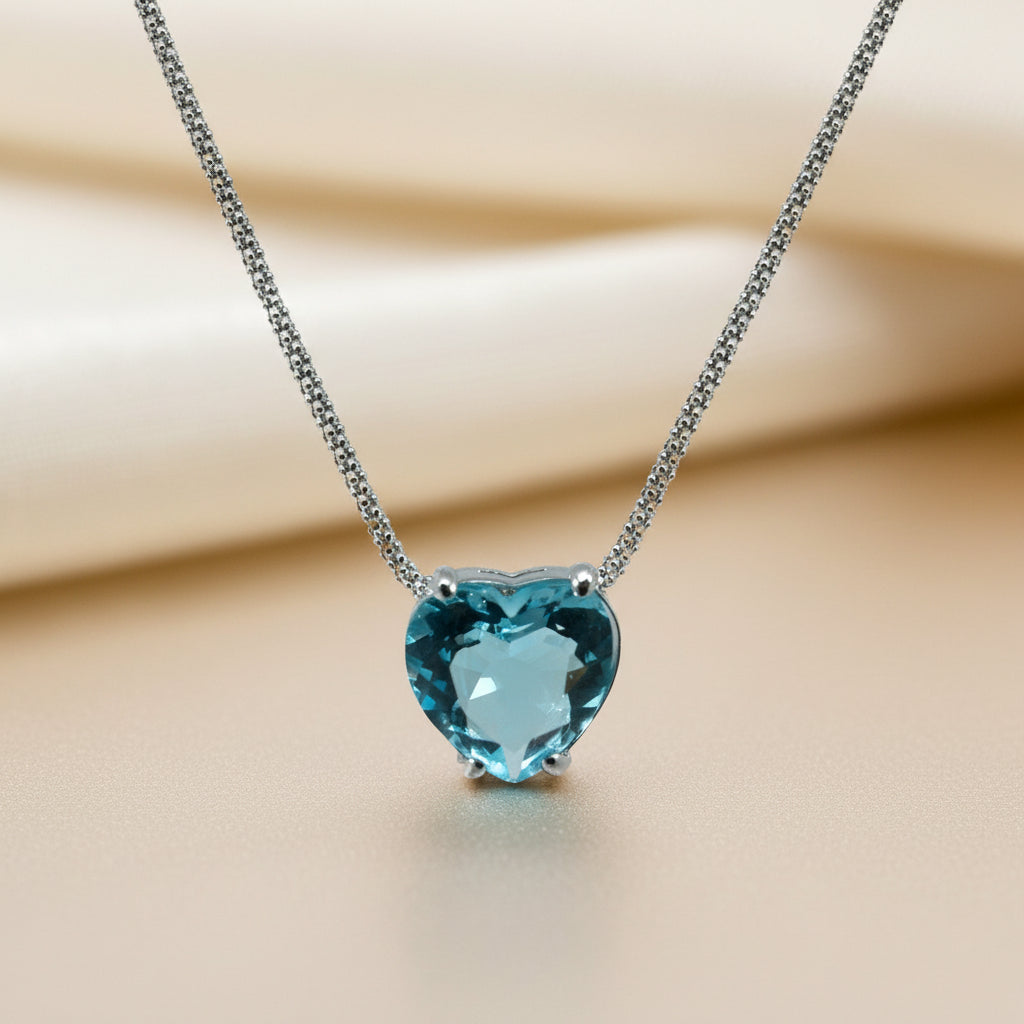 Detailaufnahme eines herzförmig facettierten Blautopas in Silber-Krappenfassung an einer feinen Silberkette.