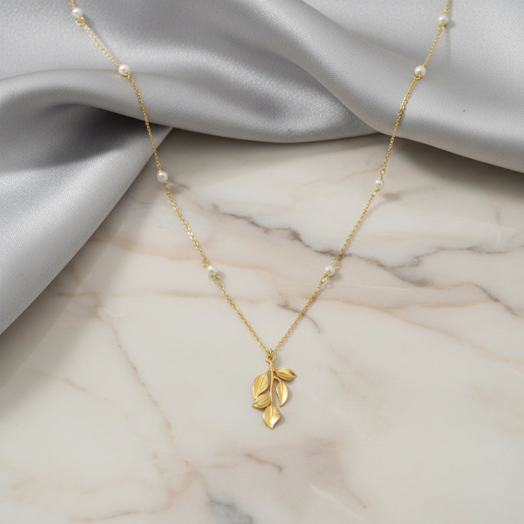 Goldene Halskette mit feinem Blätteranhänger und eingearbeiteten kleinen Perlen auf zarter Kette.