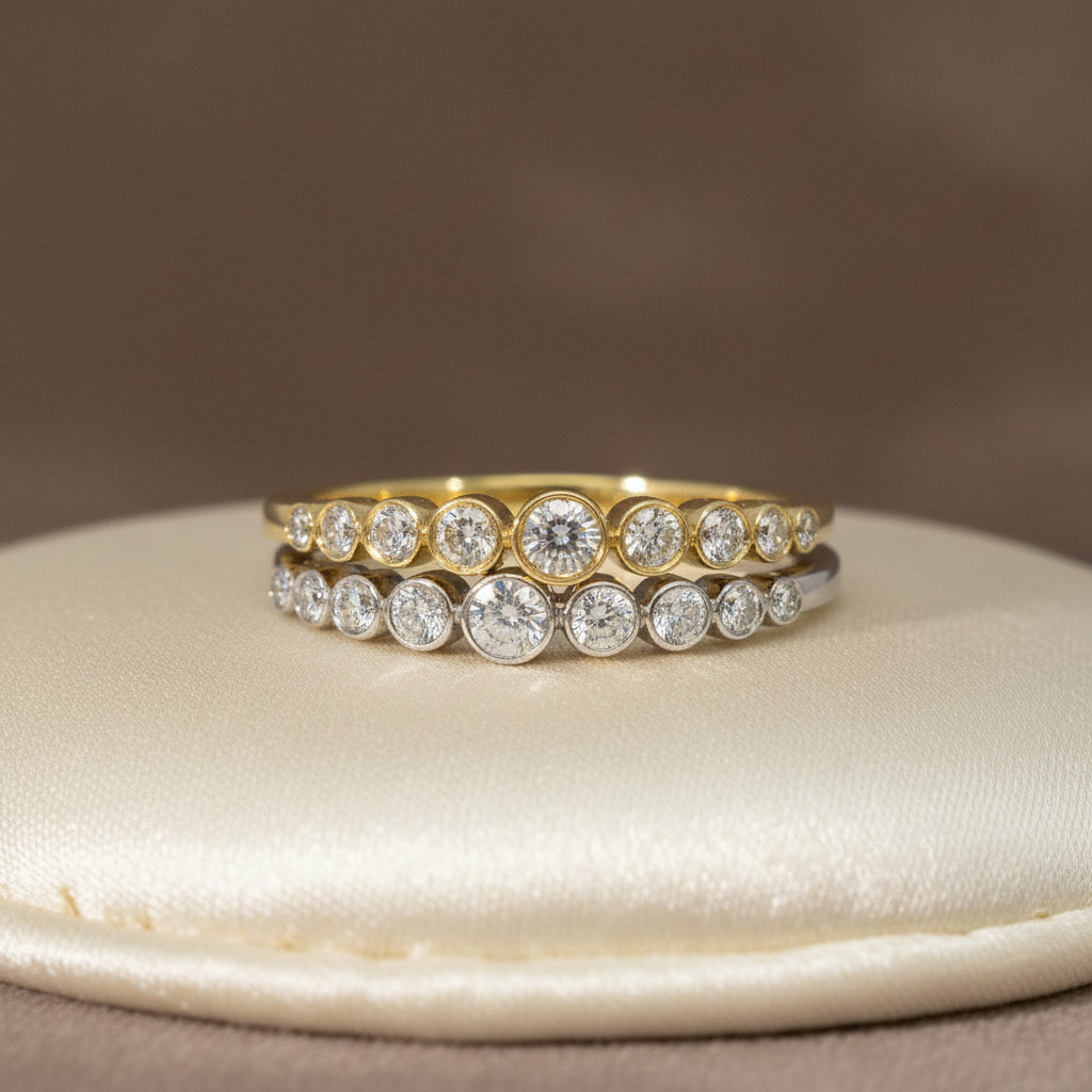 Zwei R57-Ringe in Gelb- und Weißgold nebeneinander, jeweils mit abgestufter Brillantreihe in Zargenfassung.