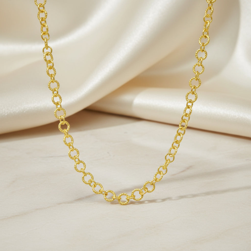 Vergoldete Gliederkette mit kleinen runden, strukturierten Kettengliedern vor weißem Hintergrund.