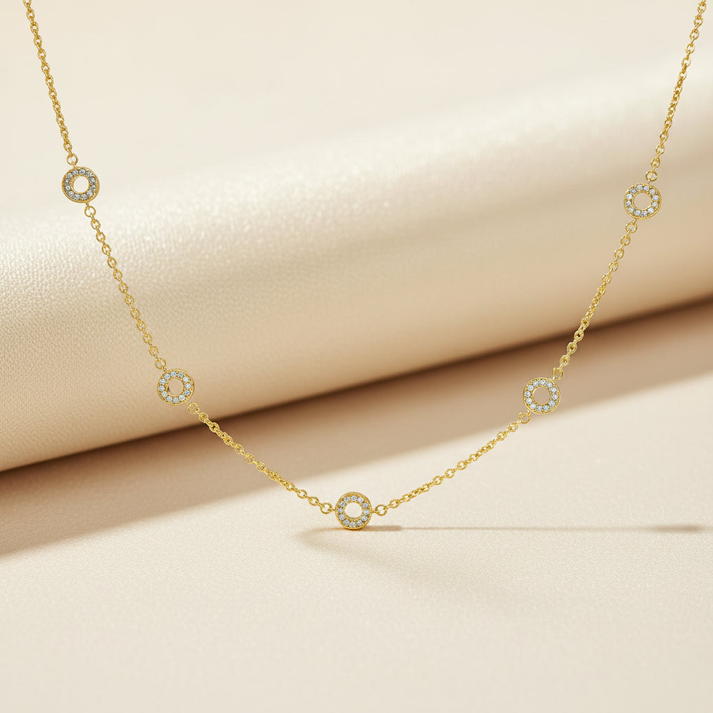 Feine vergoldete Collierkette mit mehreren kleinen, rund pavé-besetzten Zirkonia-Kreis-Elementen vor weißem Hintergrund.
